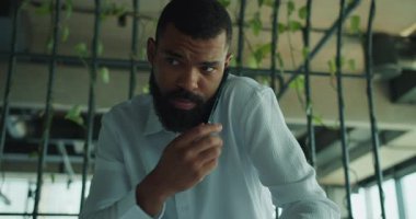 Yeşilliklerle dolu şık bir ofis ortamında bir adam odaklanmış bir telefon görüşmesi yapıyor.