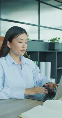 Kendini işine adamış, odaklanmış genç bir profesyonel, parlak ve çağdaş bir ofis ortamında yoğun bir şekilde dizüstü bilgisayarda yazı yazıyor.