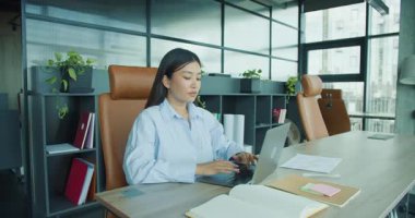 Kendini işine adamış ve odaklanmış bir birey, modern ve çağdaş bir ofis ortamında özenle bir dizüstü bilgisayarda yazı yazıyor. Yüksek kalite 4k görüntü