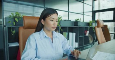 Verimliliğini arttıran şık, yeşil bir ofiste dizüstü bilgisayarı üzerinde çalışan odaklanmış profesyonel bir kadın. Yüksek kalite 4k görüntü