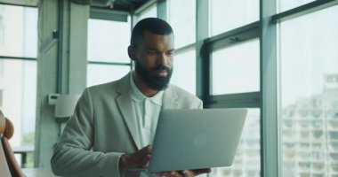 Şık bir ofis ortamında dizüstü bilgisayar kullanan odaklanmış bir profesyonel modern çalışma kültürünü sergiliyor..