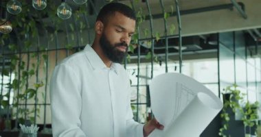 Odaklanmış bir mimar, bitkilerle dolu şık bir ofisin ayrıntılı planlarını inceliyor.