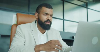 Son derece odaklanmış ve kendini işine adamış bir profesyonel, modern ofis ortamında dizüstü bilgisayar kullanıyor.