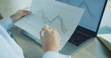 Etkili bir karşılaştırma için basılı grafikleri kullanırken dizüstü bilgisayardaki veri eğilimlerini analiz eden yetenekli bir profesyonel. Yüksek kalite 4k görüntü