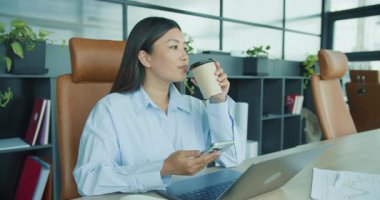 Modern ve şık bir ofis alanında, bir kadın kahvesinin tadını çıkarırken işine özenle bağlanır. Yüksek kalite 4k görüntü