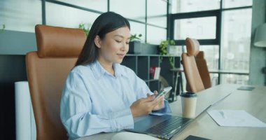 Şık bir ofis ortamında çalışan, akıllı telefonunu kullanan ve kahveden zevk alan genç profesyonel bir kadın. Yüksek kalite 4k görüntü