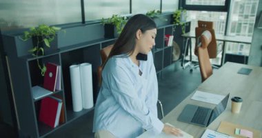 Çağdaş bir ofiste masasında belgeleri incelerken telefona odaklanmış bir profesyonel bakıyor. Yüksek kalite 4k görüntü