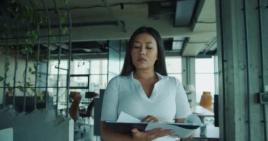 Zarif bir ofiste, doğal ışık için geniş pencereleri olan belgeleri inceleyen kendini işine adamış profesyonel bir kadın. Yüksek kalite 4k görüntü