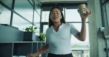 Parlak ve modern ofis ortamında neşeli bir birey elinde bir fincan kahve tutarak neşeyle dans eder. Yüksek kalite 4k görüntü