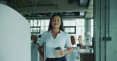 Profesyonel bir kadın, şık bir ofiste elinde kahveyle, modern çalışma alanı estetiğini sergileyerek güvenle yürür. Yüksek kalite 4k görüntü