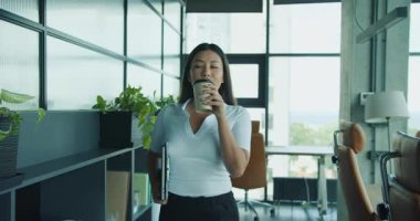 Kendine güvenen bir kadın, parlak, modern ve hayat dolu bir ofis ortamında yürürken kahvesini yudumlamaktan hoşlanır. Yüksek kalite 4k görüntü