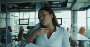 Kararlı ve odaklanmış bir kadın bir telefon görüşmesi yapıyor, profesyonelliğini şık bir ofis ortamında gösteriyor.