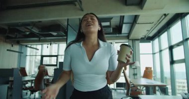 Parlak, çağdaş bir ofiste, bir kadın elinde enerji dolu bir kahve fincanı tutarken neşeyle şarkı söyler. Yüksek kalite 4k görüntü