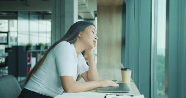 Düşünceli ve içe dönük bir kadın şık bir ofis odasında otururken derin bir yansıma yaparak pencereden dışarı bakar.,