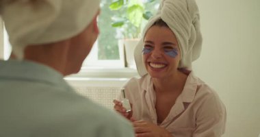 İki yakın arkadaş neşeli bir şekilde kahkahalarını evde rahatlatıcı bir spa gününde renkli yüz maskeleriyle denerken paylaşıyorlar.