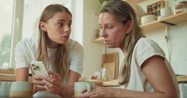 Genç bir kadın, yaşlı bir kadına telefonda ilginç bir şey gösteriyor.