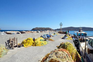 Greece, Crete, mole with fishing nets and boats in the port of Plaka with the fortress of Spinalonga, a former leper colony
