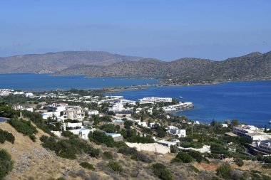 Greece, Crete, Hotel complex on the Cretan Sea with the narrow causeway to the Spinalonga peninsula, in the background the former Venetian fortress and leper island