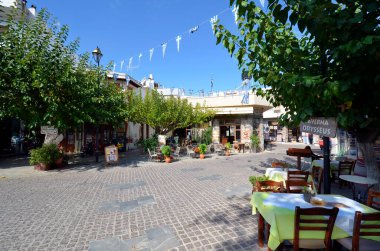 Mochos, Greece - October 11, 2022: Unidentified people on main square, is also used as meeting point with restaurants on the main square where chairs and tables are also set up outside, shops and a thoroughfare through the small mountain village on t