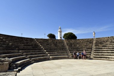 Paphos, Kıbrıs - 02 Ekim 2023: UNESCO 'nun dünya mirası sahası Kato Paphos' un arkeolojik alanındaki Odeon Amfitiyatrosu ve Paphos Lithghouse 'da kimliği belirsiz turistler, Paphos aka Pafos 2017 yılında Avrupa Kültür Başkenti oldu.