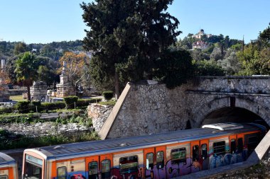 Atina, Yunanistan - 19 Aralık 2023: Metro, arka planda Ulusal Gözlemevi ve Saint Marina Kilisesi ile antik Yunan Agora boyunca uzanan tünelden geçti