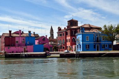 Burano, Italy - April 17, 2024: View of the colorful houses on the island in Venice Lagoon and the leaning tower of the church Chiesa Parrocchiale di San Martino Vescovo, built in 16th century clipart