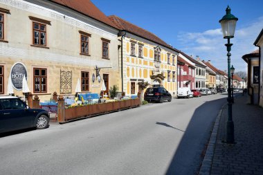 Pas, Avusturya - 23 Mart 2024: Burgenland 'daki UNESCO dünya mirası alanındaki renkli ve pitoresk evleriyle Neusiedl Gölü' ndeki sözde leylek kasabasında park arabaları bulunan ana cadde, çatıda leylek yuvaları