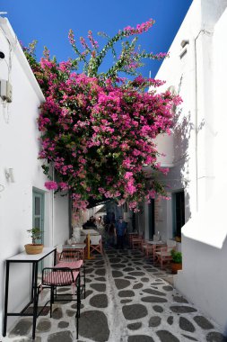 Parikia, Yunanistan - 17 Eylül 2024: Dar sokaktaki bir Yunan restoranının masaları ve sandalyeleriyle bilinmeyen kişiler geziyor