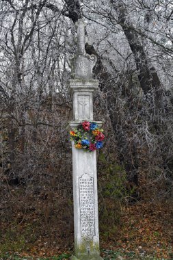Avusturya, sözde Vasperger Haçı, donla kaplı yaprak döken ağaçların kenarında çiçek çelengi olan bir tarla haçı.