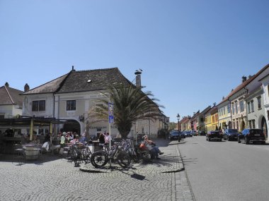 Pas, Avusturya - 20 Nisan 2025: Tanımlanamayan insanlar, Leylekler Şehri olarak da bilinen Neusiedl Gölü 'ndeki UNESCO dünya mirası sahasında, ana cadde boyunca çatısı üzerinde leylek yuvaları bulunan farklı resimli binalarla güneşli bir günün tadını çıkarıyorlar.