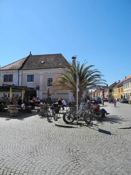 Pas, Avusturya - 20 Nisan 2025: Tanımlanamayan insanlar, Leylekler Şehri olarak da bilinen Neusiedl Gölü 'ndeki UNESCO dünya mirası sahasında, ana cadde boyunca çatısı üzerinde leylek yuvaları bulunan farklı resimli binalarla güneşli bir günün tadını çıkarıyorlar.