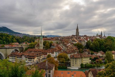 Bern 'ün mavi güneşli gökyüzünün altında panoramik manzarası, İsviçre' deki güzel Aare Nehri 'nin kucakladığı, eski kasabadaki kırmızı çatılı evlerin arasında duran Bakanlığın Gotik kulesi.