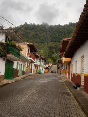 Jerico, Antioquia, Kolombiya - 5 Nisan 2022: Gri Tuğla Sokağı Şelaleli Dağlara Karşı Renkli Evler