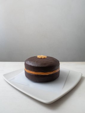 Fıstık ezmeli vejetaryen çikolatalı kek. Çikolatalı kremayla kaplanmış. Beyaz arka planda küçük fıstıklarla süslenmiş.