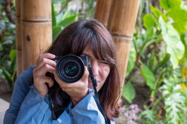 Mavi ceketli, boynuna askılı bir kamera takmış genç bir kahverengi kadın yağmurlu bir günde, Telephoto Angle 'da bambu direkleri ile fotoğraf çekiyor.