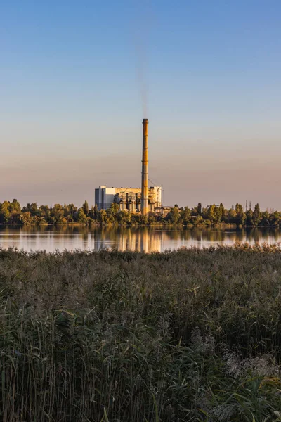 Amid a colorful sunset sky, the chimneys of waste processing plants at a lake emit air pollution. Energy generated from waste comes at the cost of environmental pollution.