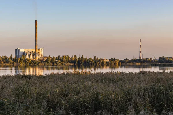 Waste processing plants on a lake bank, their chimneys billowing smoke, generate energy from waste. But environmental pollution, including air pollution, is an unfortunate side effect.