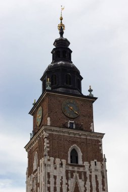 Krakow Belediye Binası Kulesi 'nin detaylı görüntüsü, bulutlu bir gökyüzüne karşı saat yüzü, tuğla işçiliği ve mimari özelliklerini gözler önüne seriyor. Polonya 'nın tarihi simgesi.