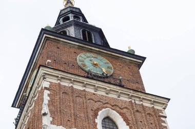 Krakow Belediye Binası 'nın alçak açılı görüntüsü saat yüzünü ve mimari detayları vurguluyor. Açık gökyüzüne karşı tuğla ve taş yapı. Polonya 'nın Krakow kentindeki tarihi eser.