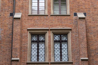 Eski bir tuğla binanın yakın çekim görüntüsü. Karmaşık pencere ızgaraları, kemerli tuğla işçiliği ve dekoratif taş elementler..