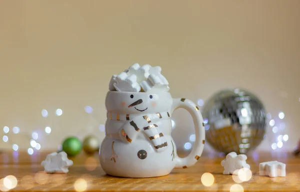 お祝いの光を背景にテーブルの上に白いマシュマロを乗せた雪だるまの形をしたカップ — ストック写真