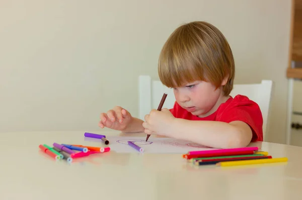a cute little boy tries to draw with colored pencils