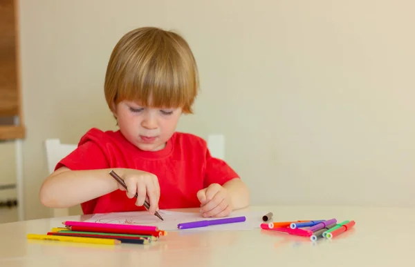 child boy draws with colored pencils while sitting at the table. childhood, development, education, leisure.