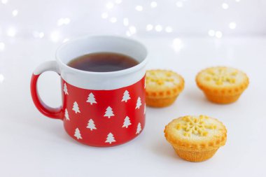 red cup with fir trees and mini cakes with snowflake on the table clipart