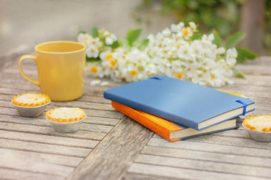 Kitaplar ve fincanlar bahçede beyaz çiçeklerle masada.