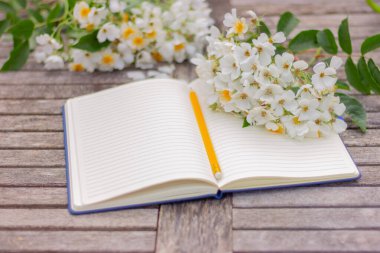 Boş sayfaları ve bahçedeki tahta masada beyaz çiçekleri olan açık bir defter.
