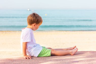 Bir çocuk deniz kıyısında oturuyor, yan manzara