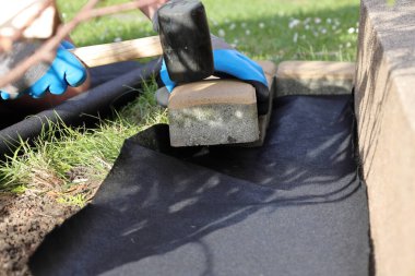 Bahçeye anti-ot paspası sermek, kaldırım taşları ve dekoratif çakıl taşlarıyla birlikte.