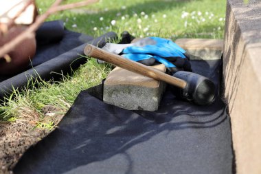 Bahçeye anti-ot paspası sermek, kaldırım taşları ve dekoratif çakıl taşlarıyla birlikte.