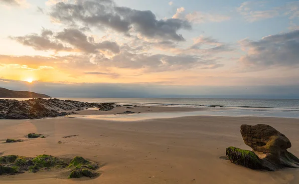 Sunrise, rocks on the beach, with golden sand, golden light reflected in the wet sand, peaceful tranquil scene.